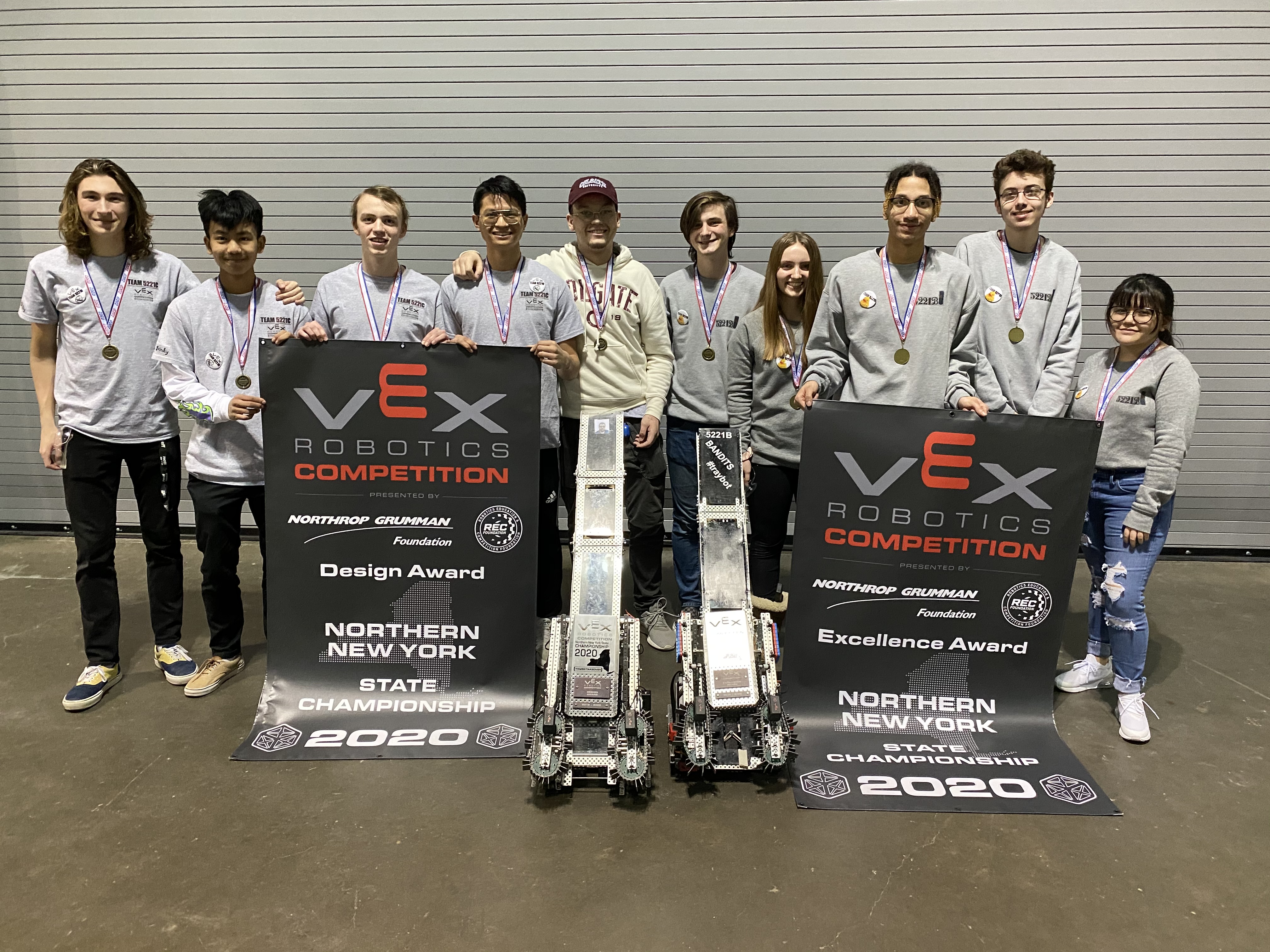 This is a photo of a group of Corcoran VEX students standing in a line, smiling as they hold VEX Championship signs.