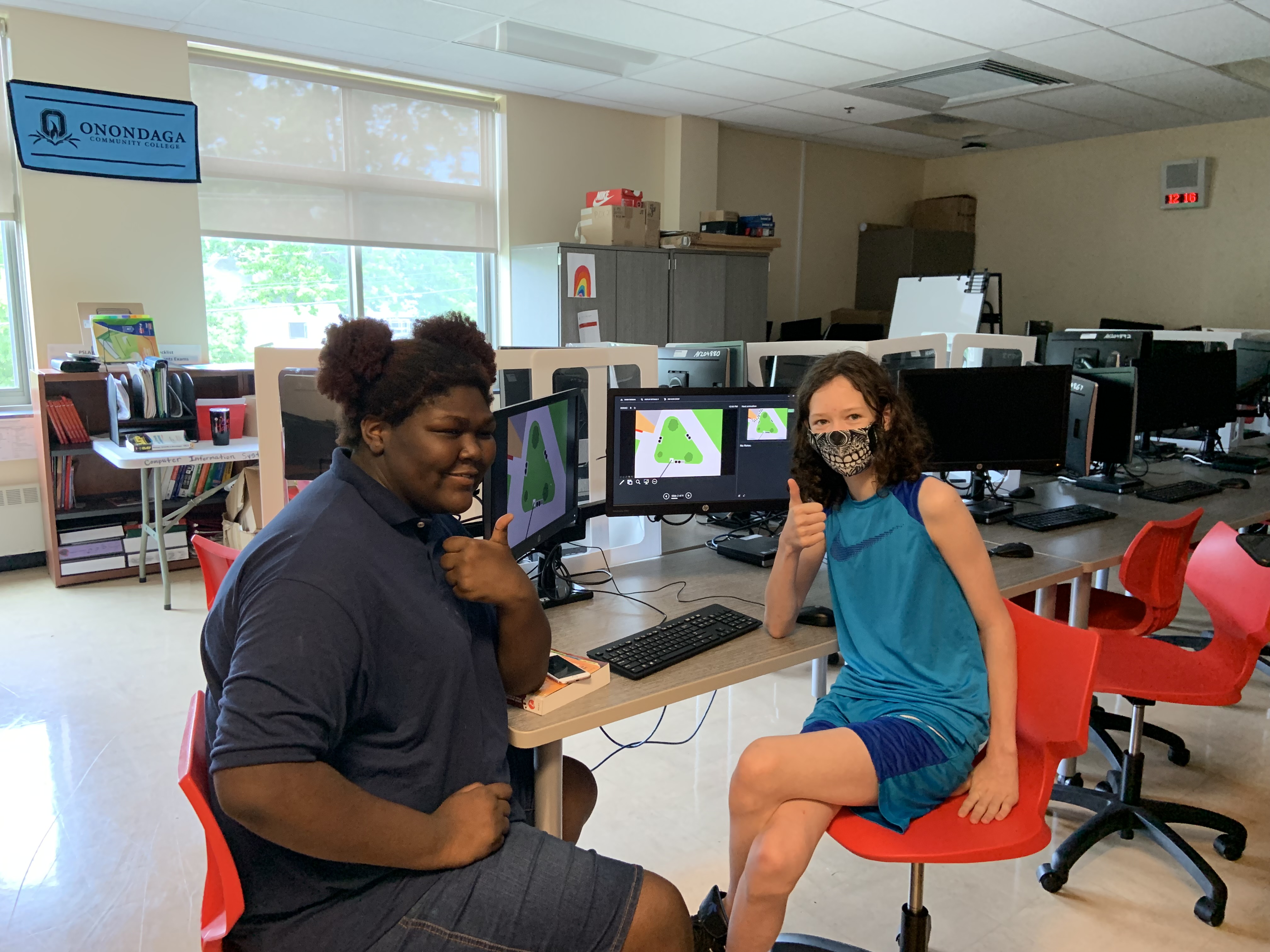 This is a photo of two PSLA students sitting next to a computer smiling at the camera while giving 'thumbs up' signals