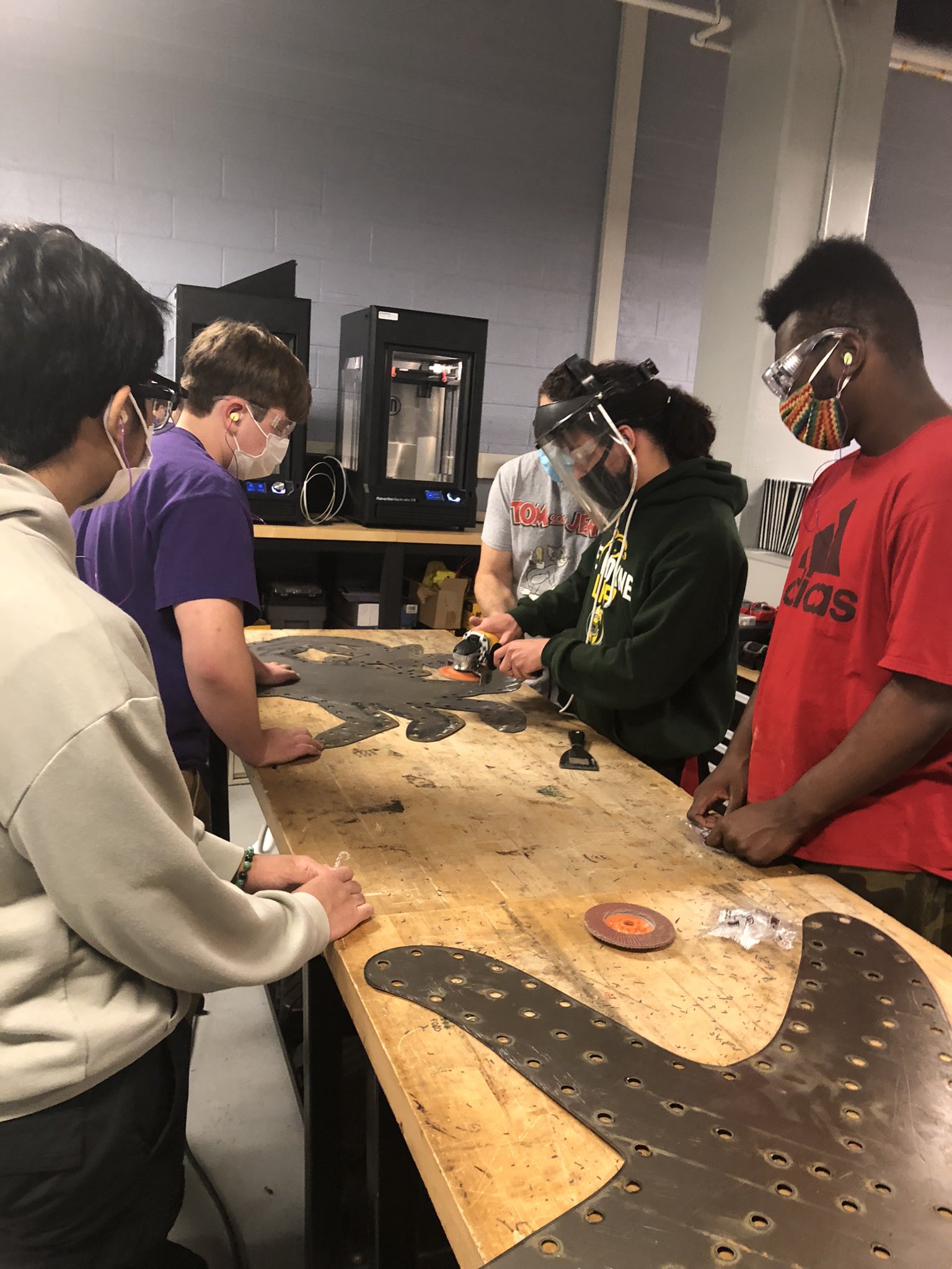 This is a photo of four students gathered around a table looking at a steel cutout of an animal they designed for a light display at the Zoo.