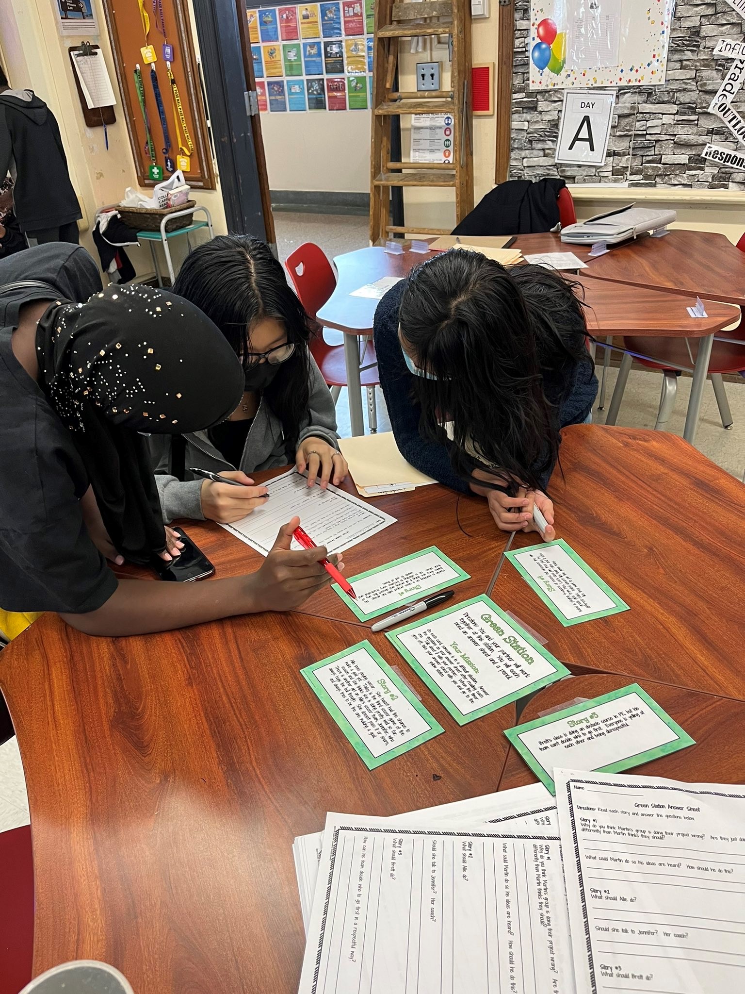 This is a photo of three students huddled around a table, looking at a piece of paper.