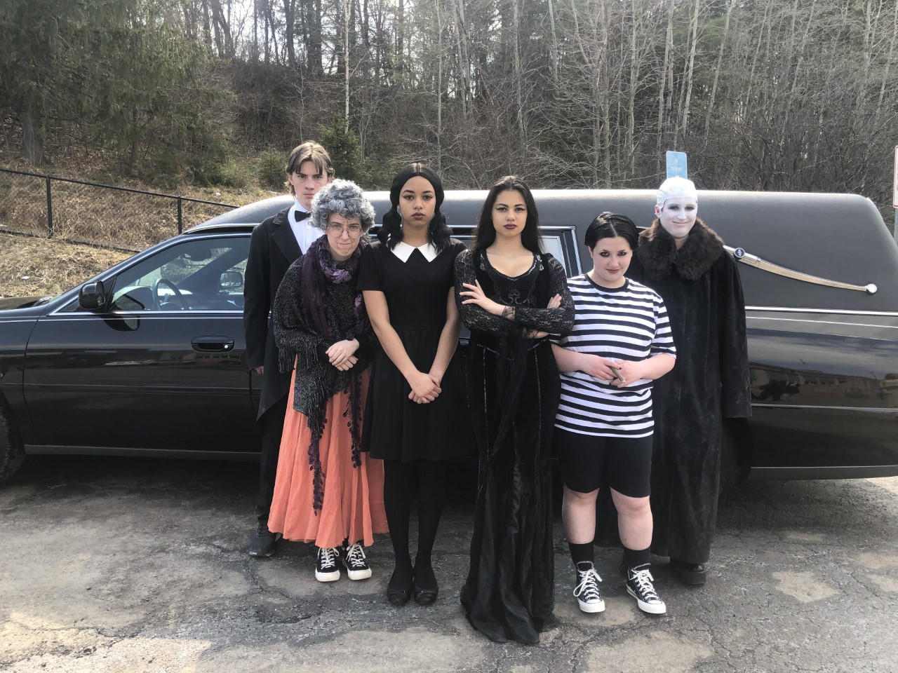 This is a photo of the lead cast members in The Addams Family, all dressed in costume and standing in front of a black car.