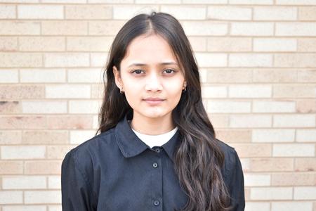 This is a photo of ITC Salutatorian Maya Dhakal standing in front of a brick wall, smiling at the camera.