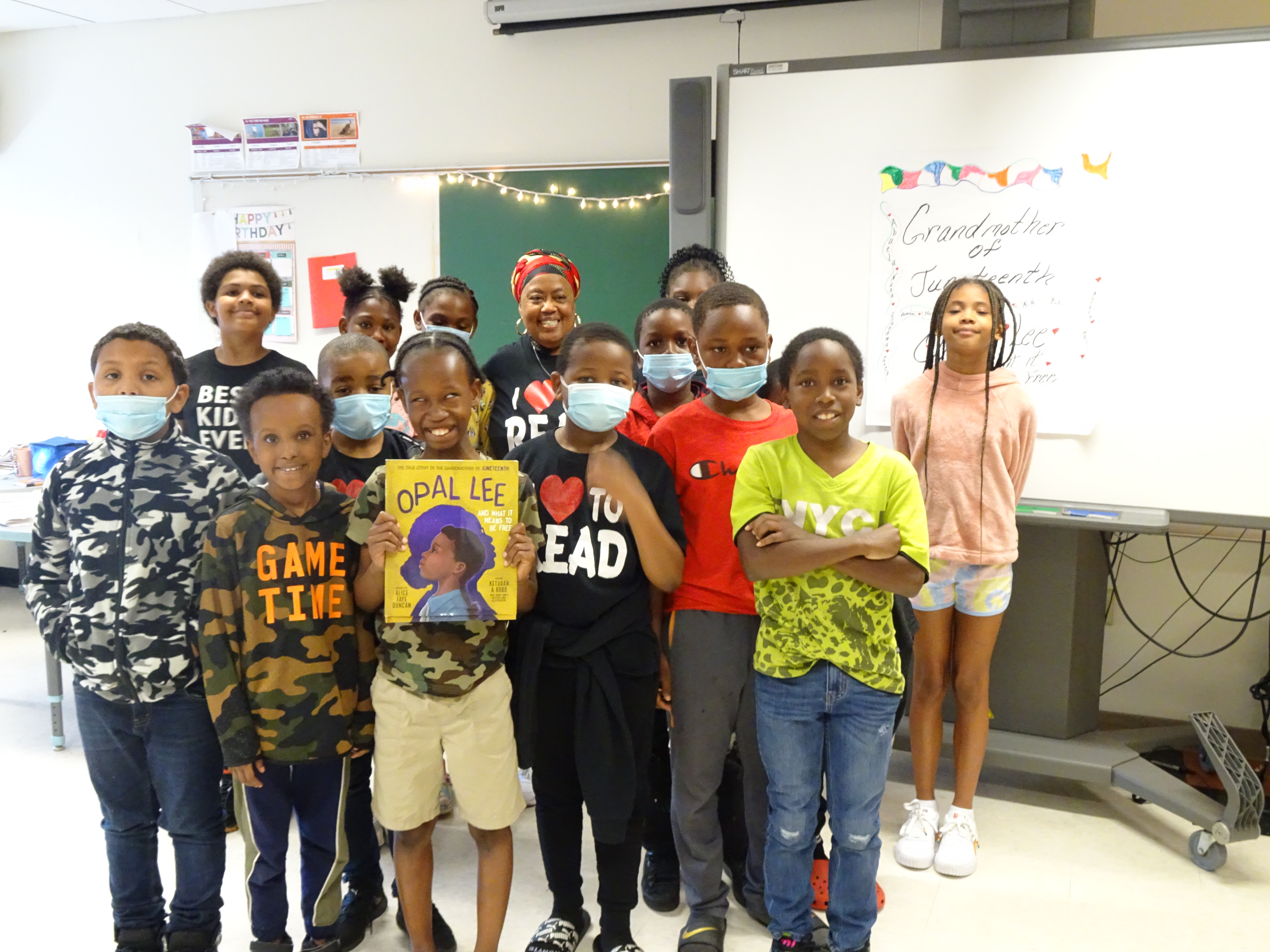 This is a photo of students in Ms. Pace's class standing in front of a sign reading 'Opal Lee: Juneteenth's Grandmother" and holding a book about Opal Lee.