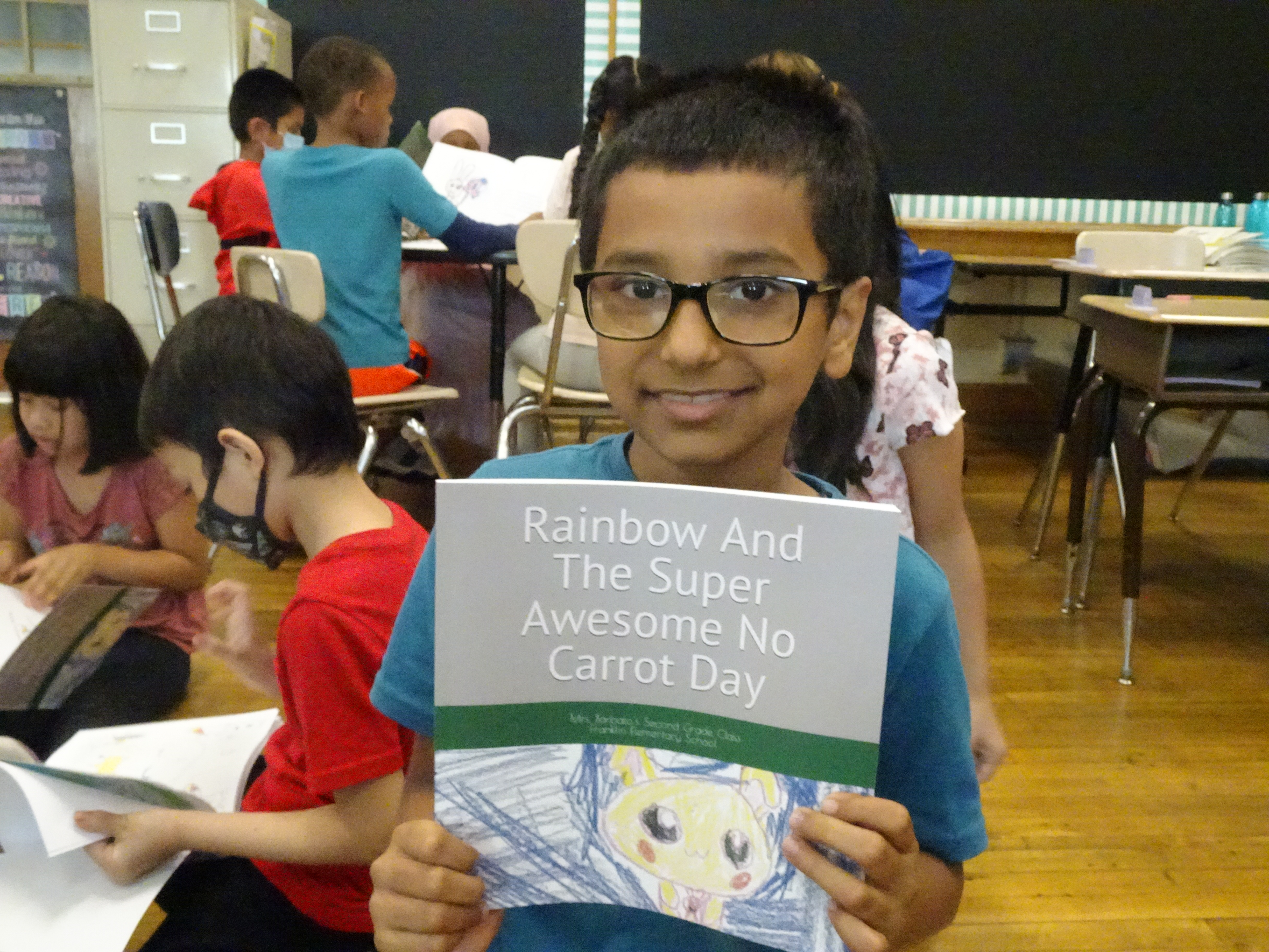 This is a photo of a boy holding a copy of the book 'Rainbow And the Super Awesome No Carrot Day.' 