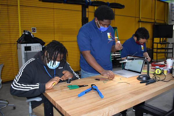 This is a photo of three students standing over a work bench, each working on an electrical task.