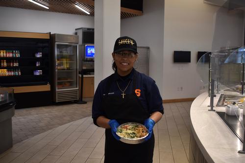 This is a photo of a SCSD student standing in an empty Syracuse University dining hall, holding a salad.