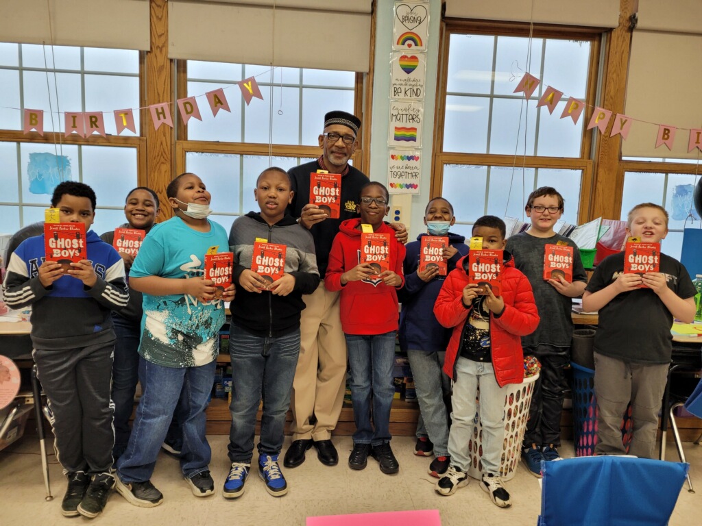 This is a photo of a group of boys standing in a line in front of a classroom window, each holding a copy of a book.