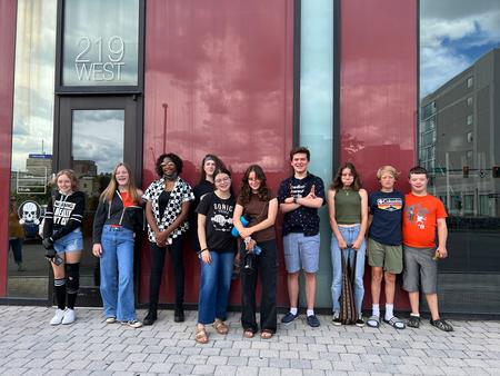 This is a photo of a group of SCSD students standing in front of a wall outside a building in downtown Syracuse, smiling at the camera.