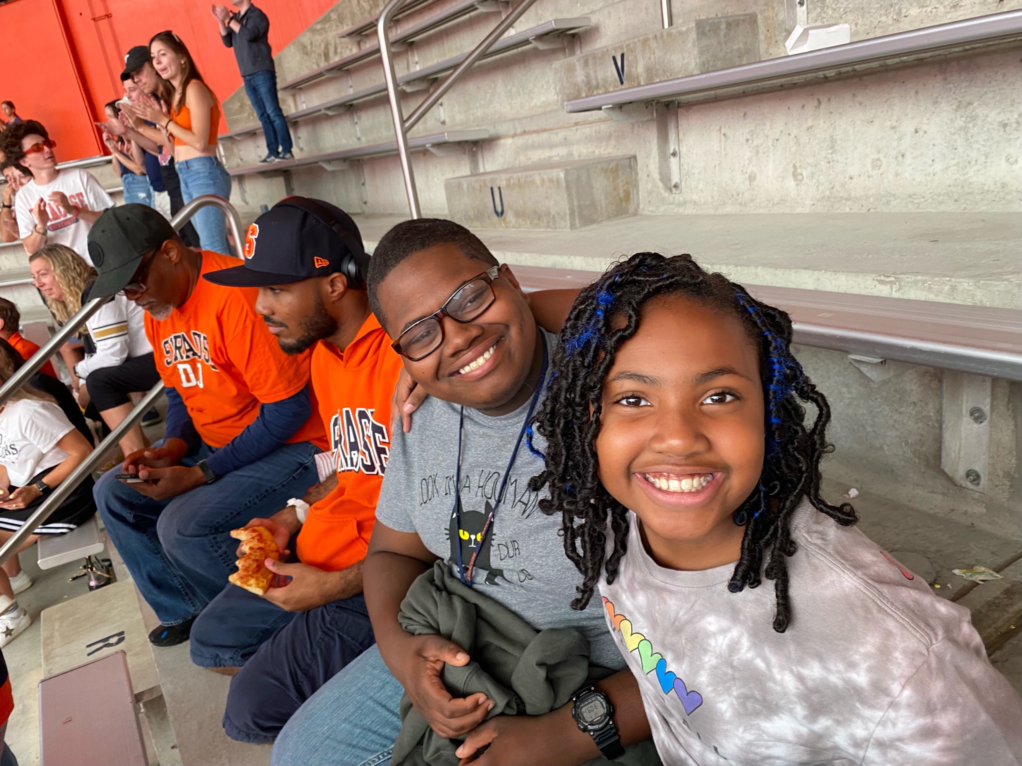 This is a photo of two OnCampus students smiling at the camera while sitting in the stands at an SU game.