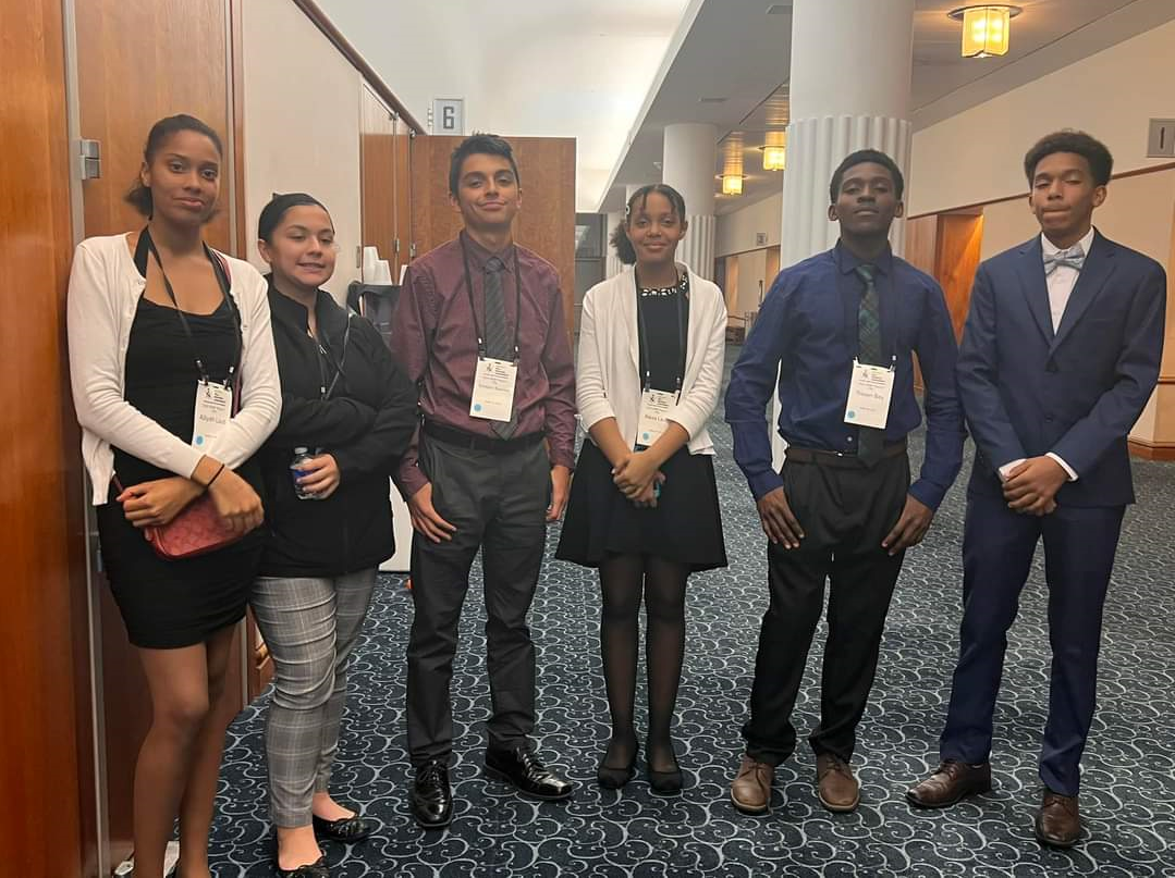 This is a photo of six students standing in a line smiling at the camera.