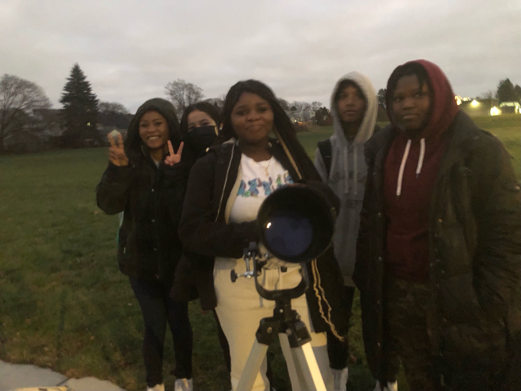 This is a photo of five Grant students standing next to a telescope outside their school building.