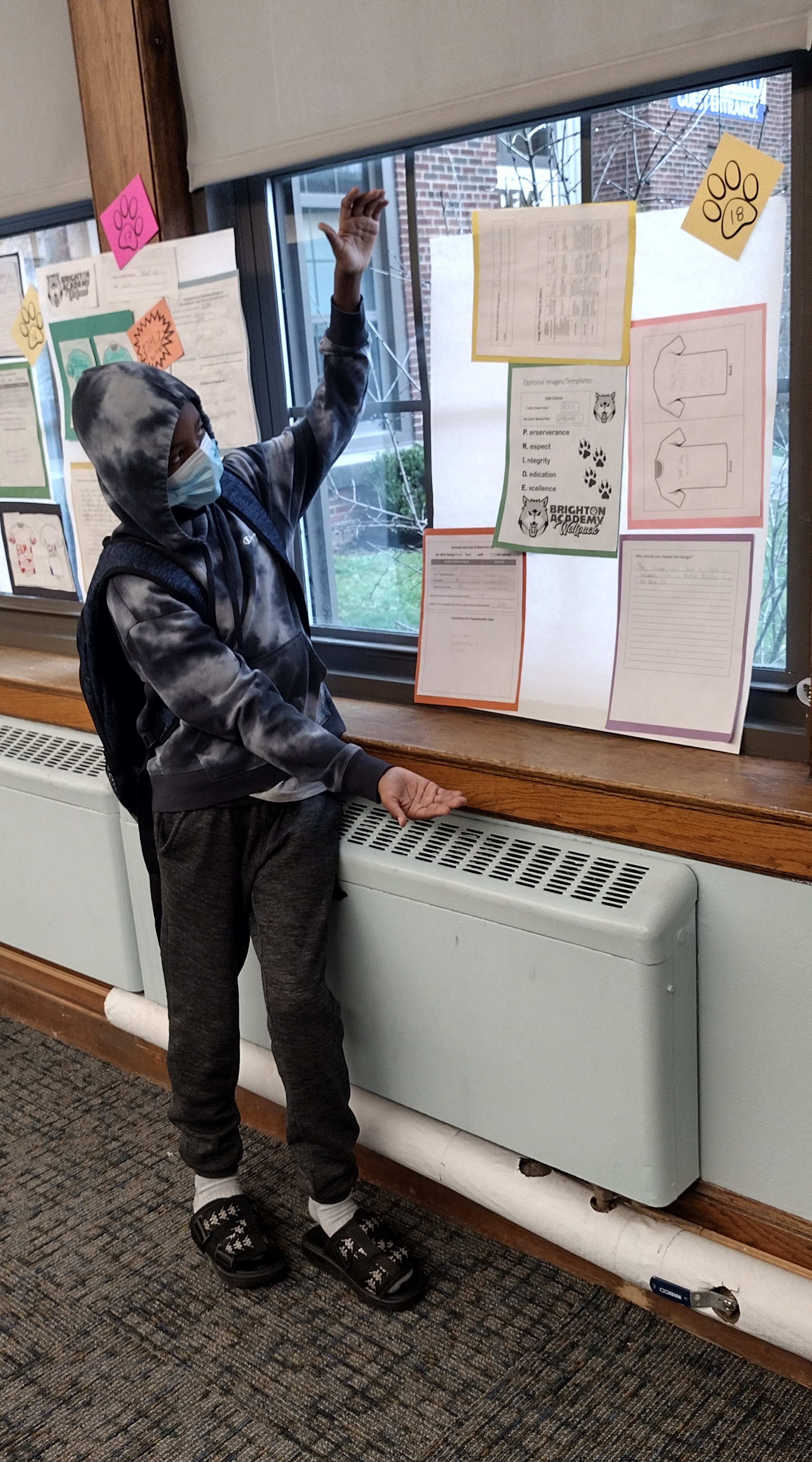 This is a photo of a male student wearing a hoodie, standing next to a posterboard with his project displayed. 