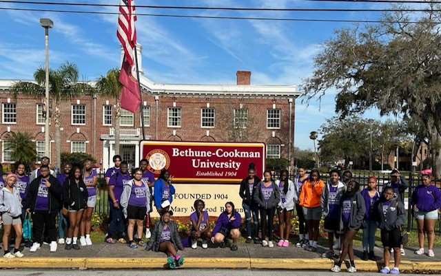 This is a photo of a group of students gathered around a sign for Bethune-Cookman University. 