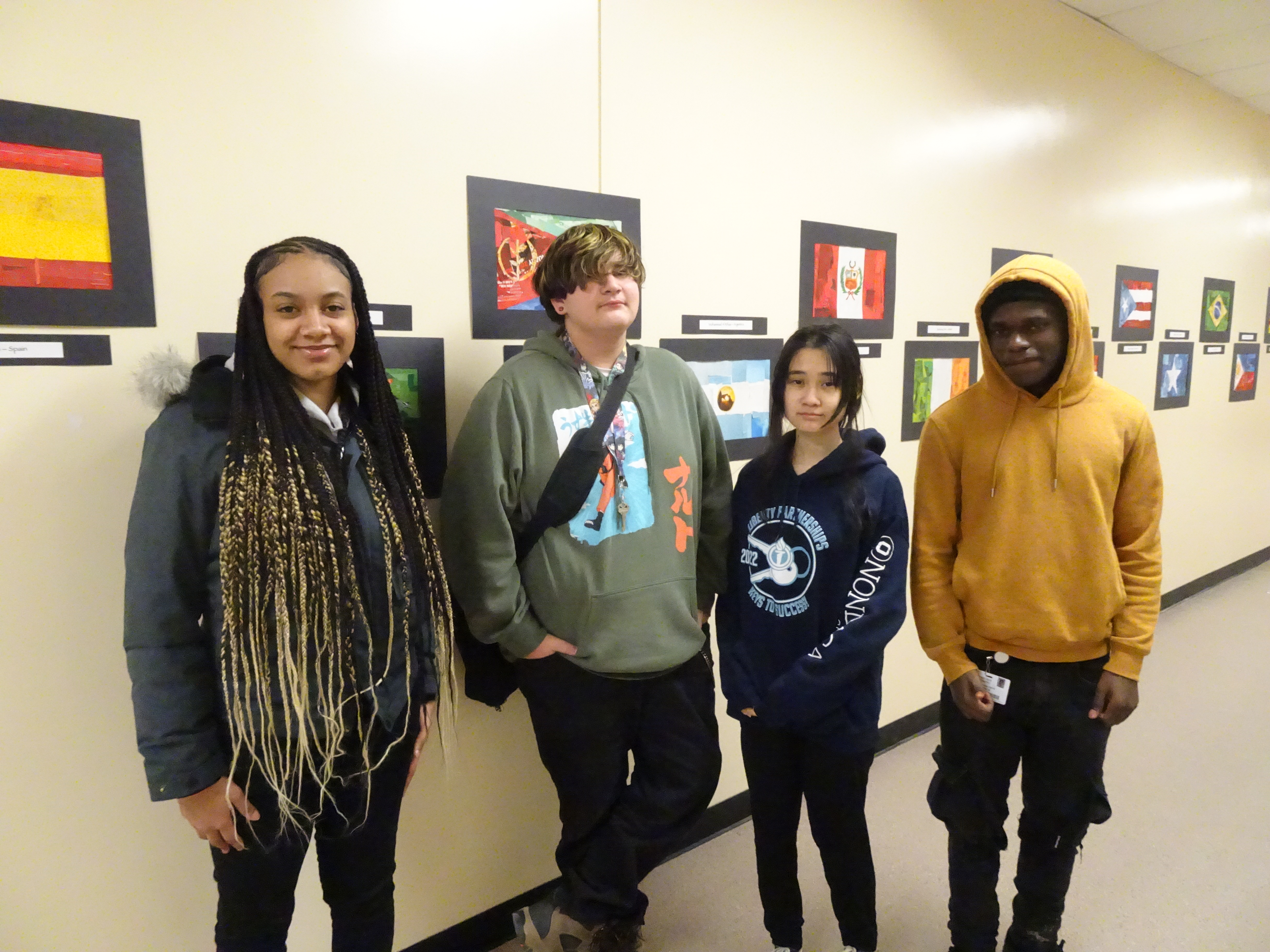 This is a photo of four PSLA students standing in a hallway in front of artwork hanging on the wall, individual student flag creations.