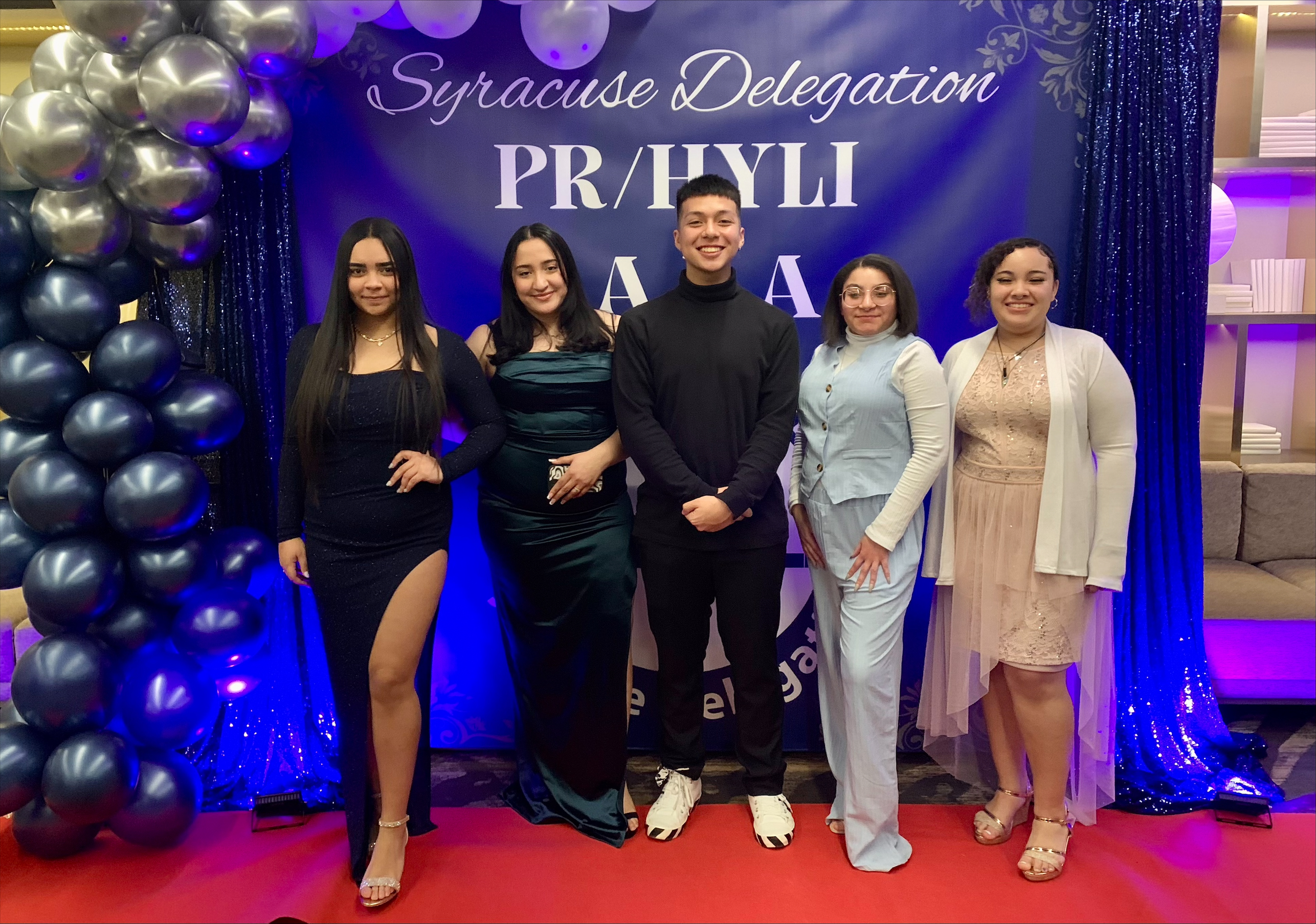 This is a photo of five SCSD students who attended the PRHYLI, standing in front of a balloon arch dressed up and smiling at the camera.