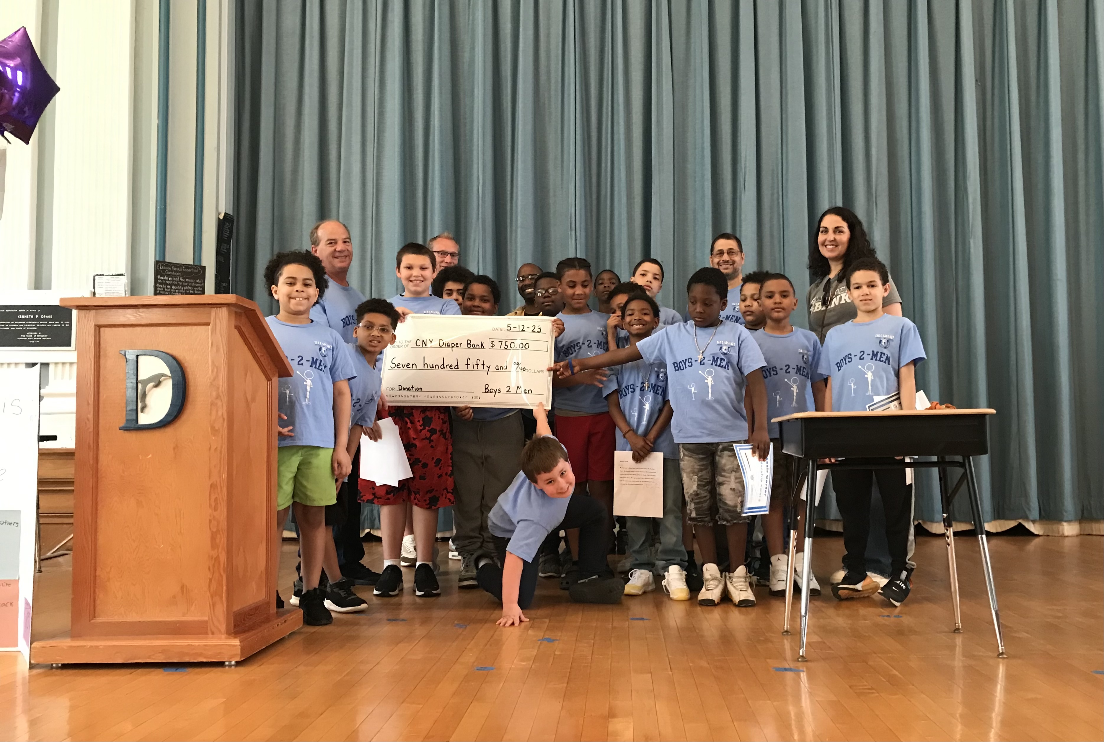 This is a photo of a group of Delaware Primary School students standing on their school stage holding a large check and smiling for the camera.