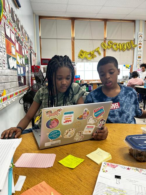 This is a photo of two Van Duyn students sitting at a table in their classroom,  looking at a laptop.