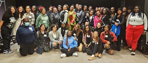 This is a photo of a group of young women attending the Sisters Empowering Sisters conference, all standing together surrounding one of the motivational speakers and smiling for the camera.