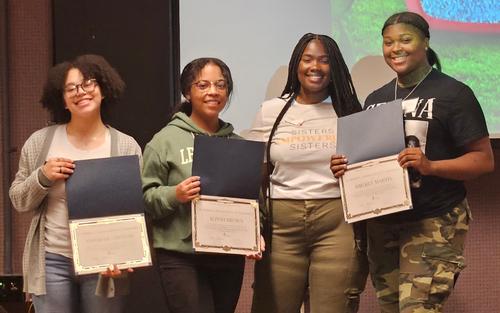 This is a photo of three ITC students, each holding a scholarship certificate, smiling at the camera as they pose with a mentor at the Sisters Empowering Sisters conference.