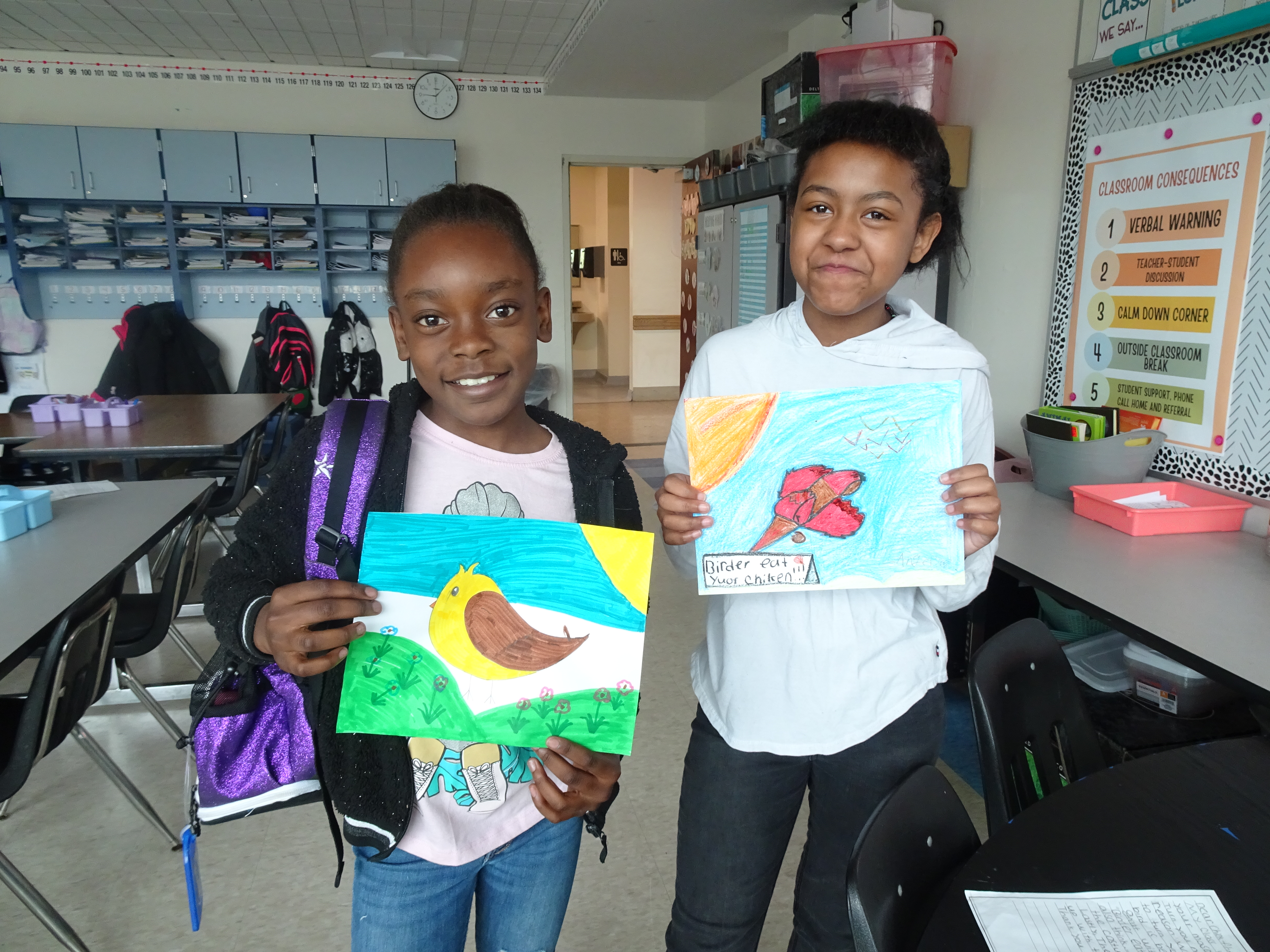 This is a photo of two McKinley-Brighton students holding artwork they drew and smiling at the camera.