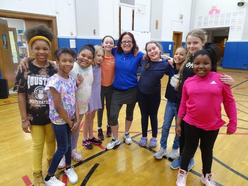 This is a photo of a group of Syracuse Latin students and their gym teacher, huddled together in the school gym and smiling at the camera.