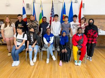 This is a photo of a group of Grant Middle School students smiling at the camera as they stand in front of a line of flags representing other nations.