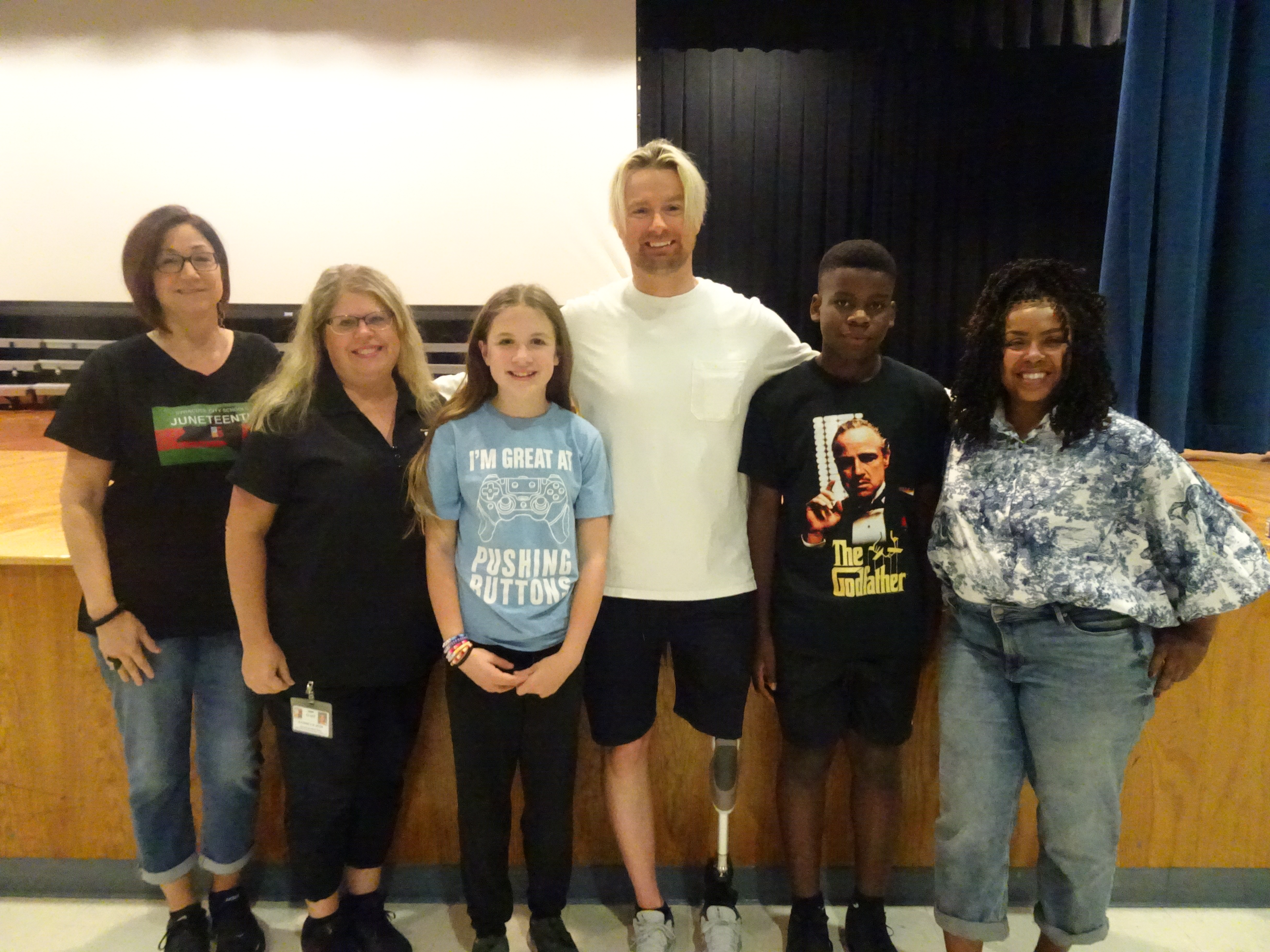This is a photo of two HW Smith students, standing alongside a motivational speaker and three GEAR UP staff members in their school auditorium.