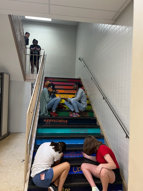This is a photo of students sitting on a staircase at Corcoran high school, painting the treads of the stairs with positive messages.