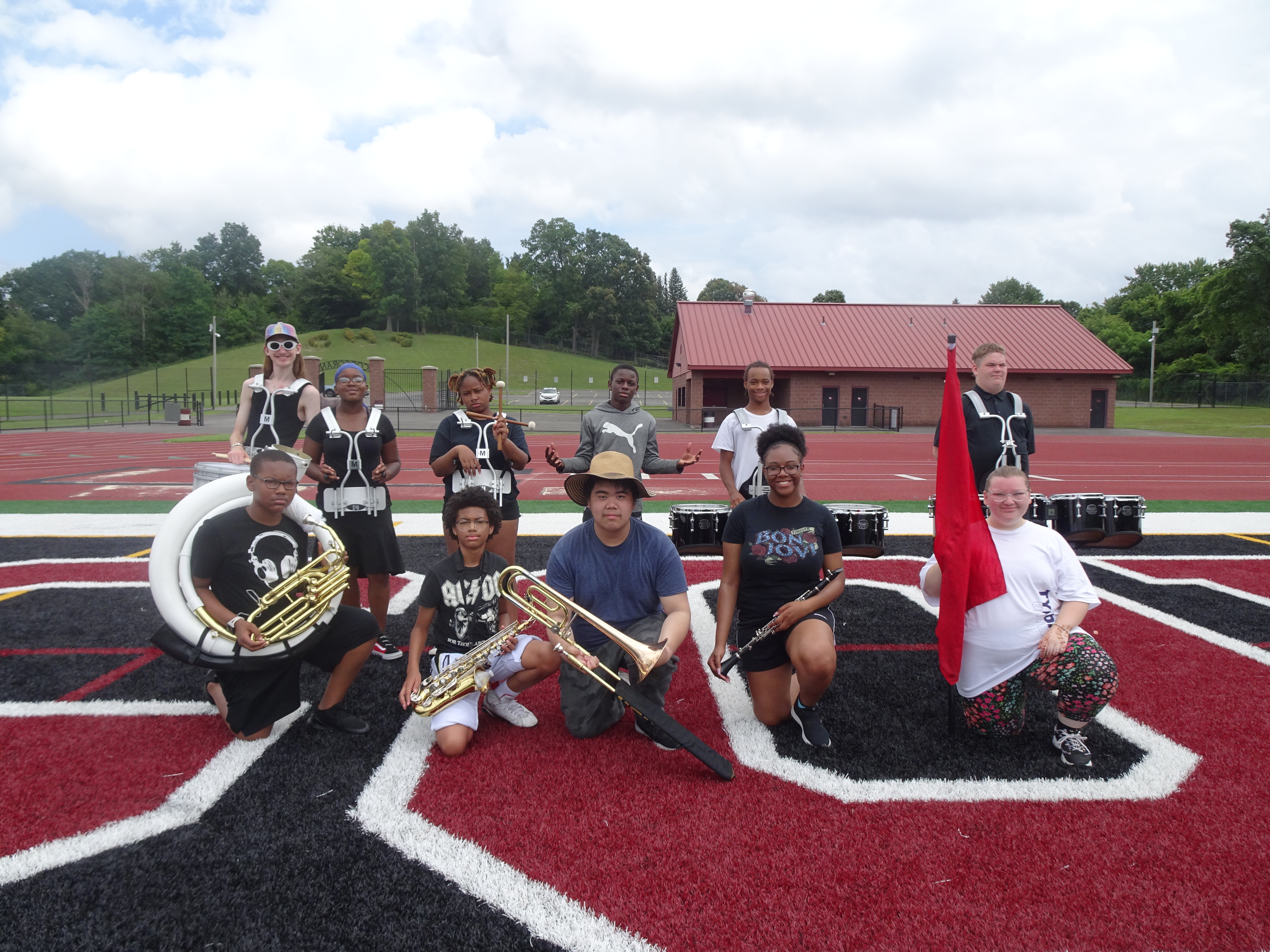 This is a photo of the SCSD Summer Marching Band students, lined up in two rows and standing in the endzone of the Corcoran football field, each holding their musical instrument.