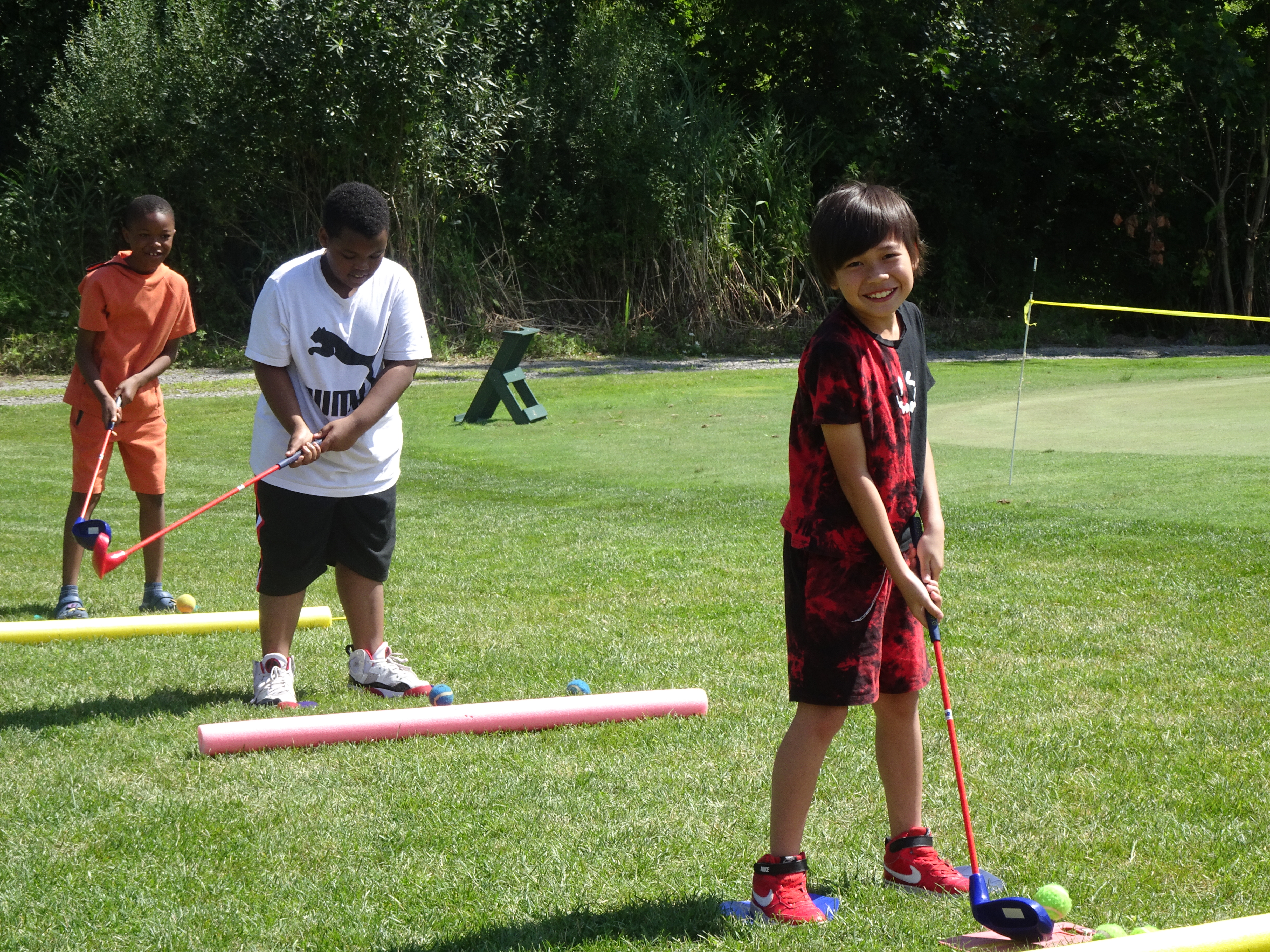 This is a photo of three students standing on a putting green swinging the golf club and smiling at the camera.