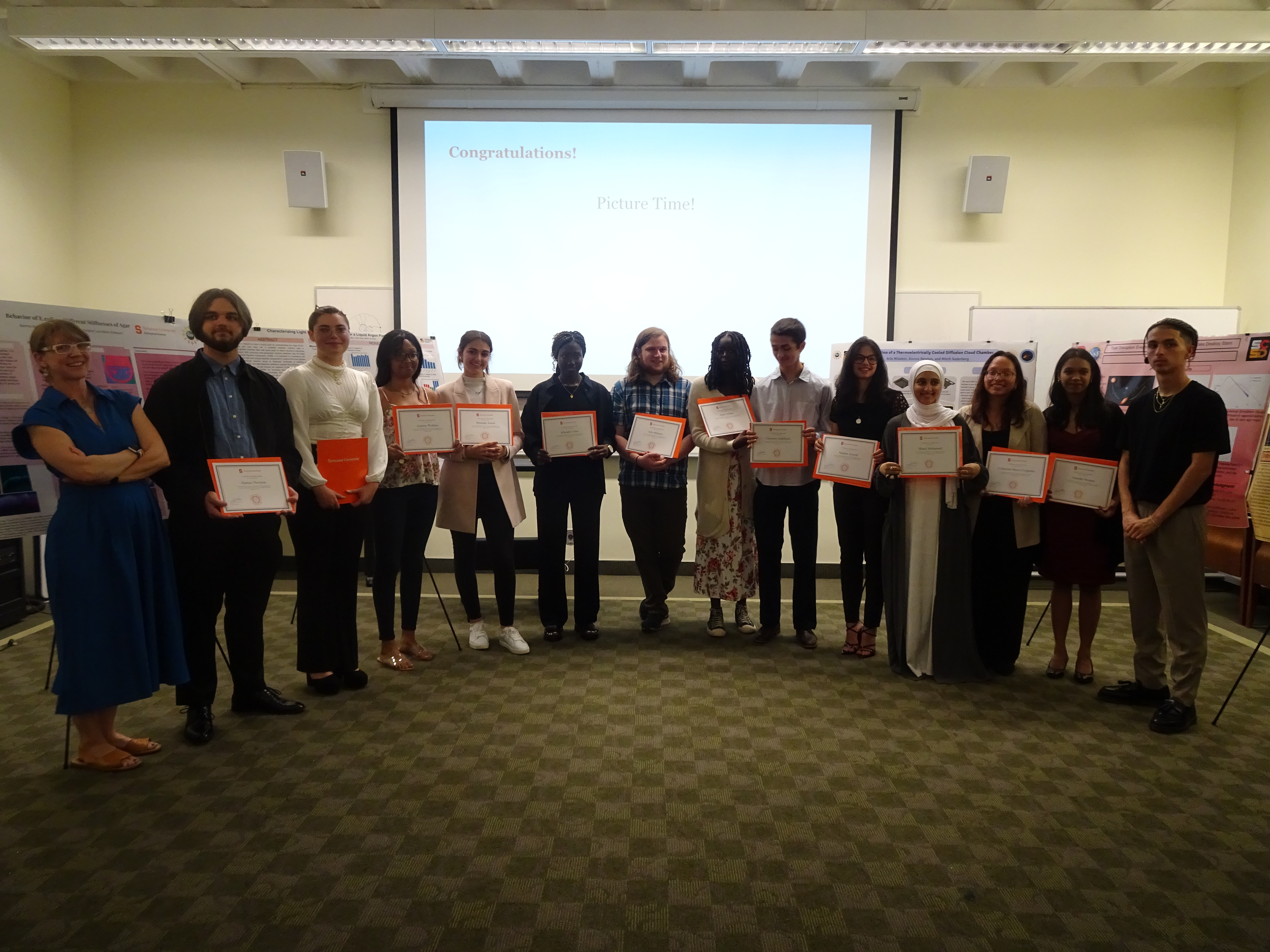 This is a photo of a group of SU Physics interns, standing in a row, each holding a certificate of achievement.