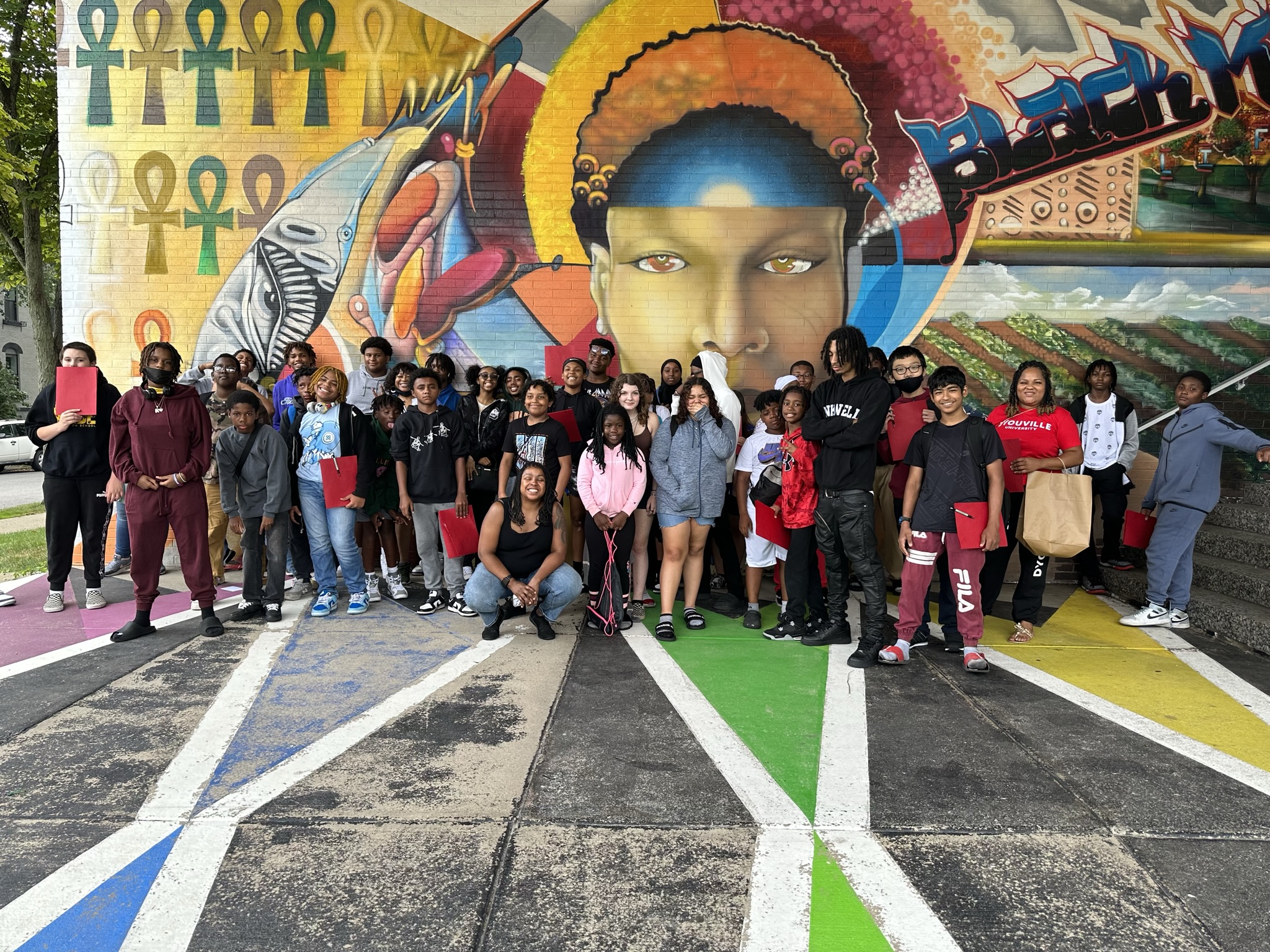 This is a photo of a group of GEAR UP students, standing in front of a wall mural and smiling at the camera.