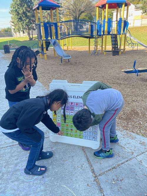 This is a photo of three boys on the Dr. Weeks playground pointing to icons on a sandwich board.