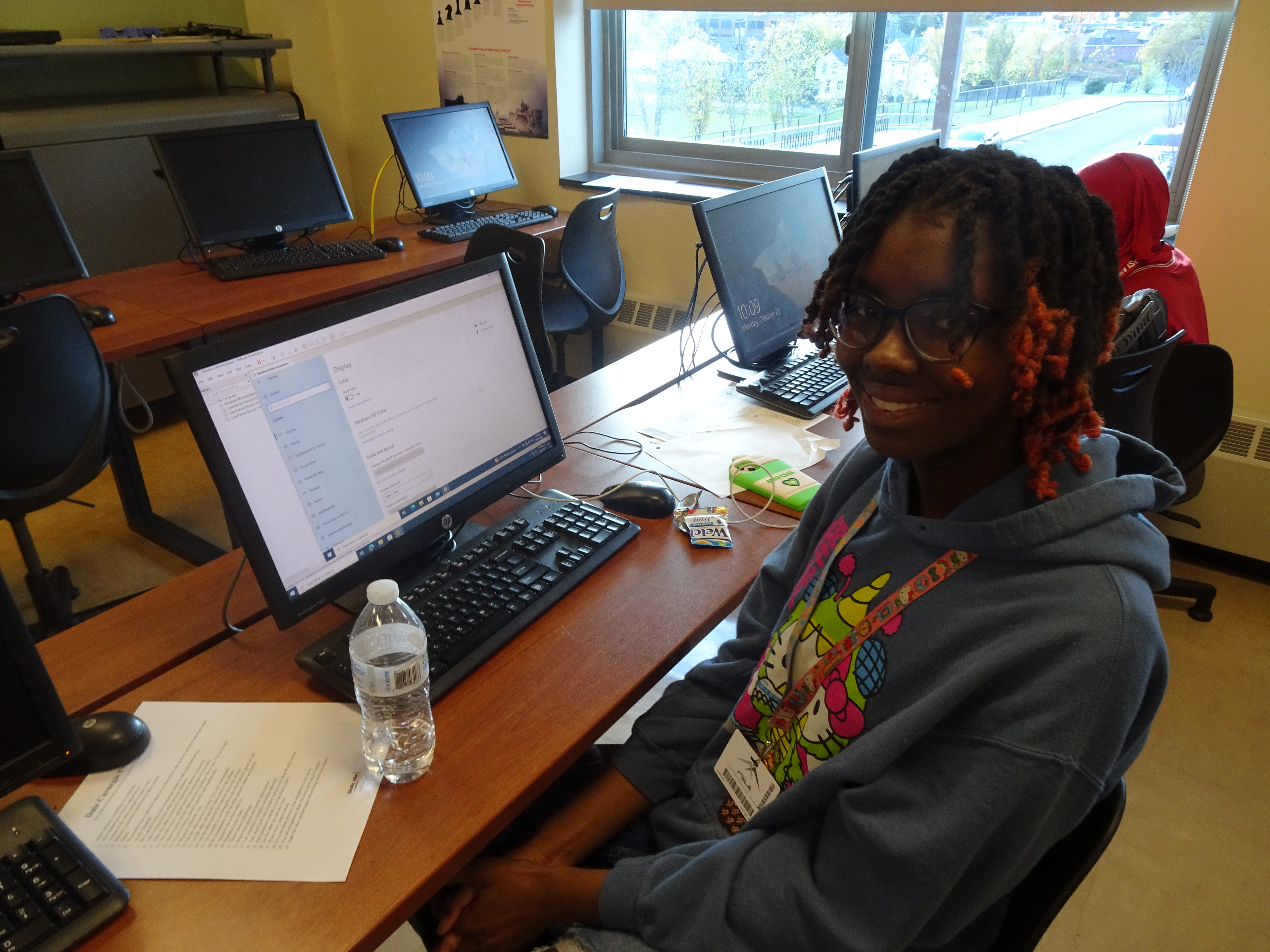 This is a photo of a PSLA at Fowler student sitting at a computer and smiling at the camera.