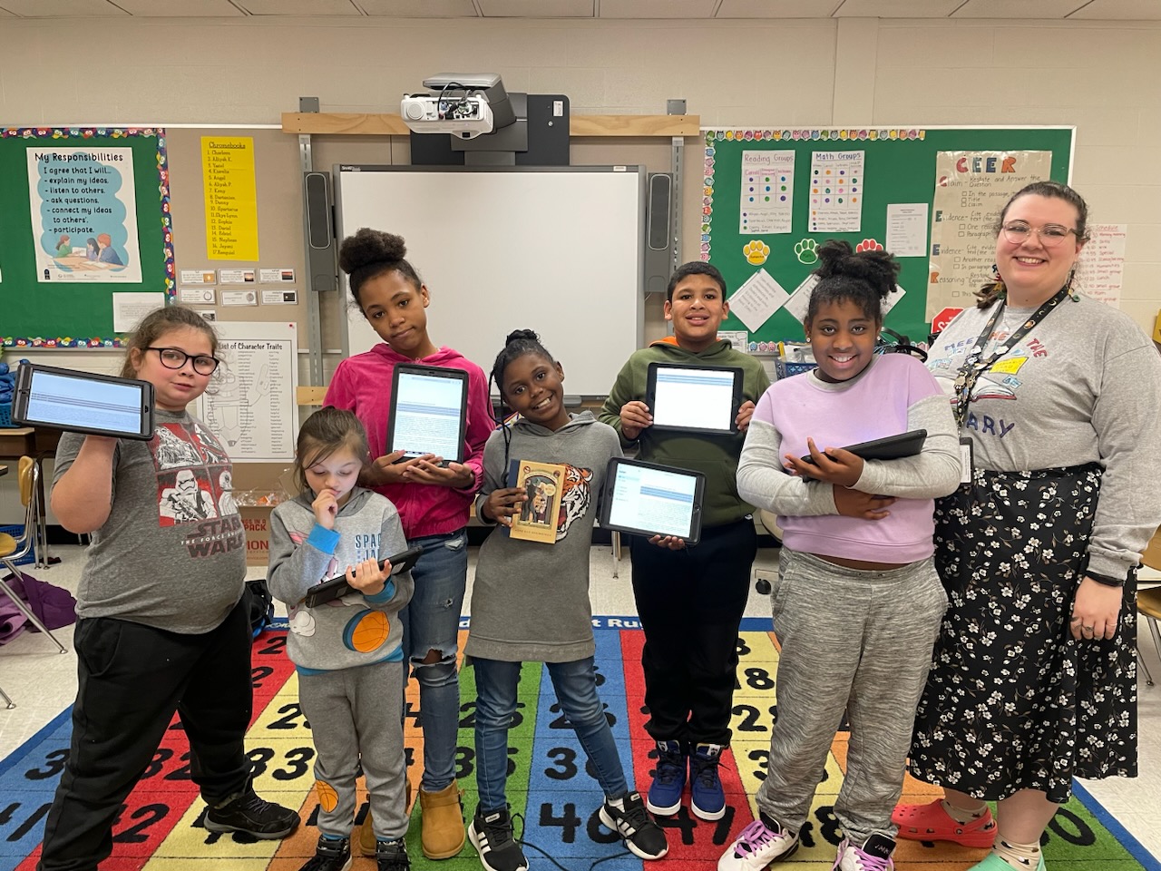 This is a photo of a group of Delaware students holding their digital devices or books and smiling at the camera.