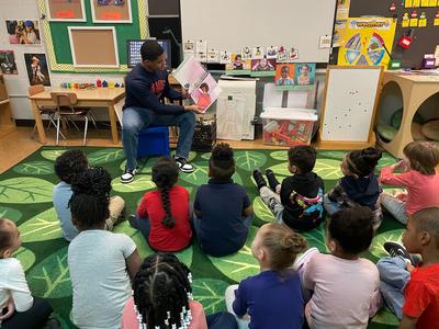 This is a photo of a Syracuse University football player reading to a group of Huntington kindergarten students.