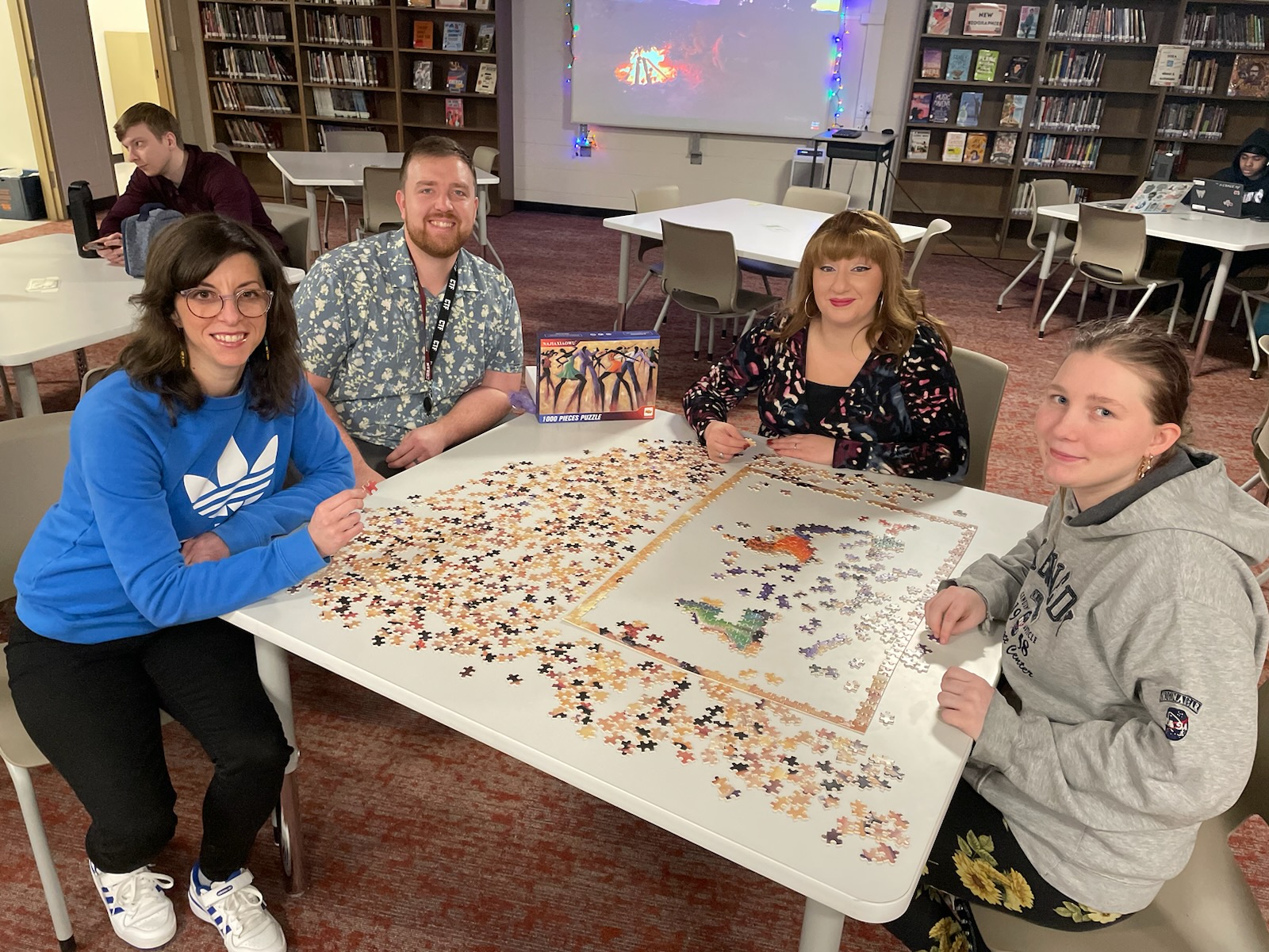 This is a photo of three staff members and a student sitting around a table with a puzzle on the top and smiling at the camera.