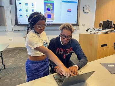 This is a photo of a student pointing to a computer screen with a mentor looking on.