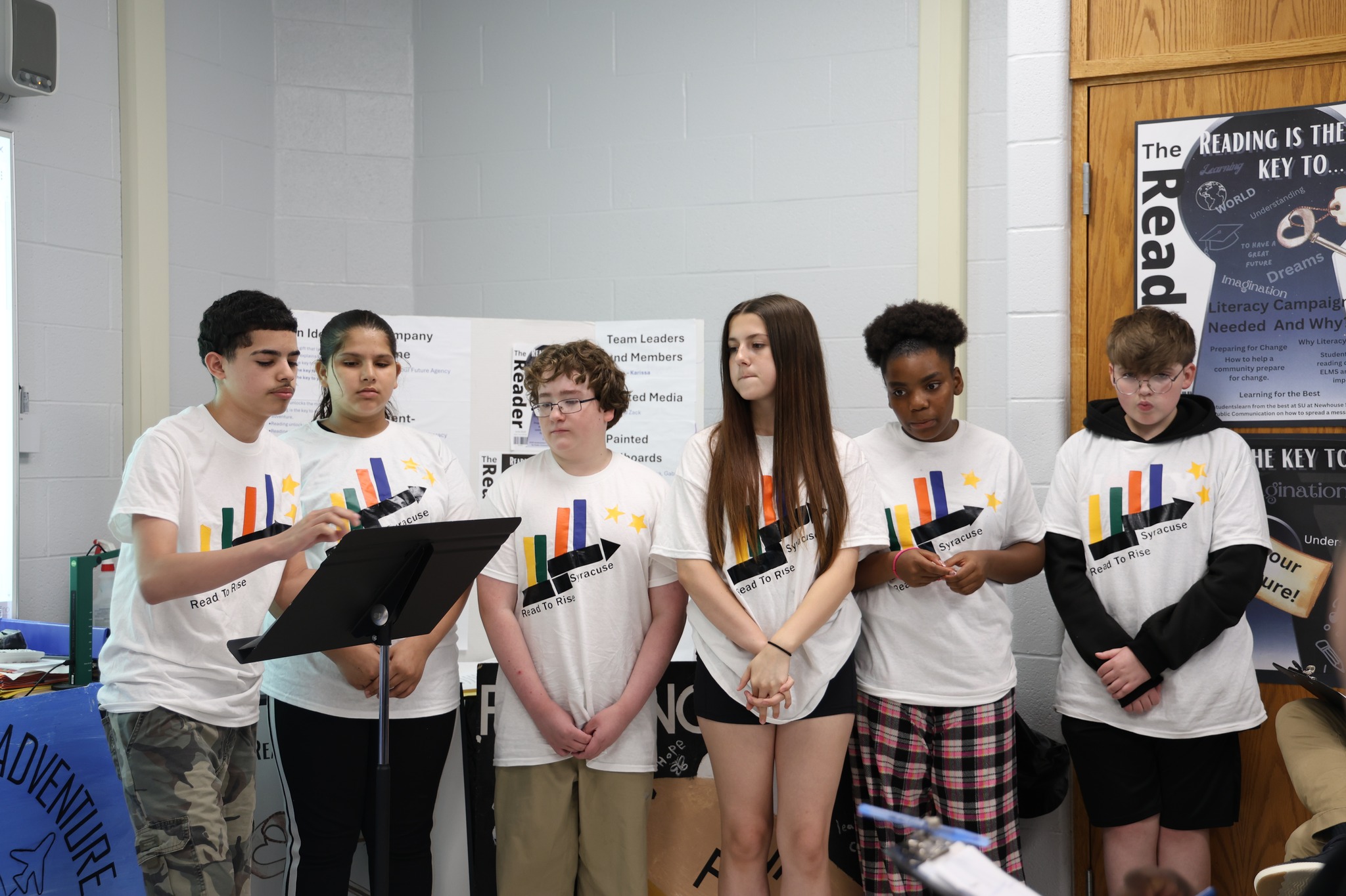 This is a photo of a group of ELMS students standing in front of a classroom in matching tshirts to present their ideas on Pitch Day.