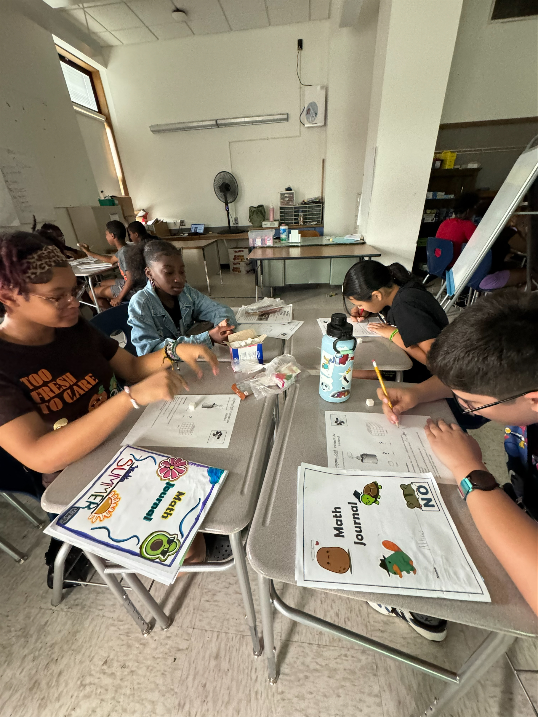 This is a photo of four students sitting at a table and completing math worksheets.