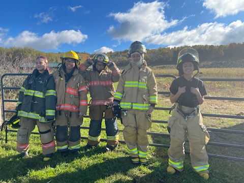 This is a photo of five PSLA Fire Rescue students, in full fire uniforms, standing alongside a fence at Springside Farm.