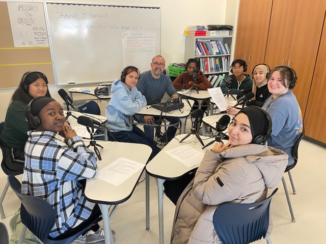 This is a photo of Henninger students sitting in front of microphones and smiling at the camera.