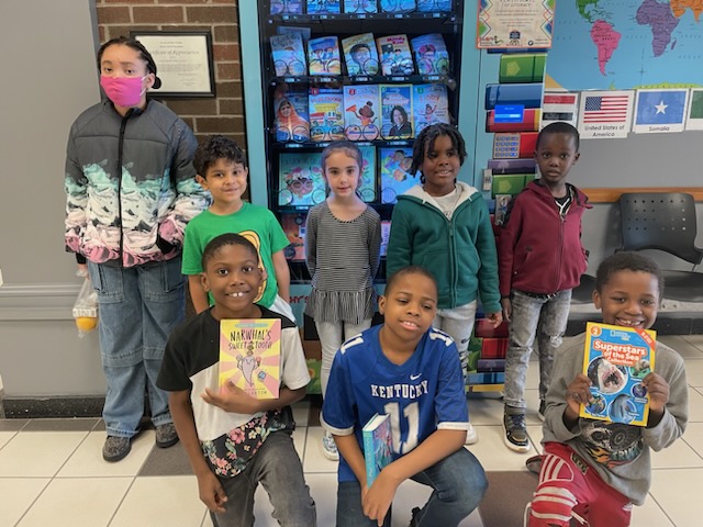 This is a photo of a group of students standing in front of a book vending machine and smiling at the camera.