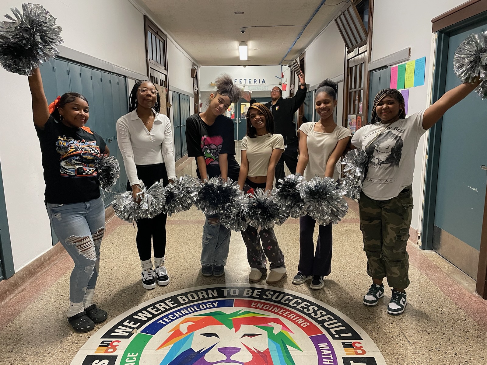 This is a photo of members of the Syracuse STEM at Blodgett cheer team standing in the school hallway posing with their pom poms.