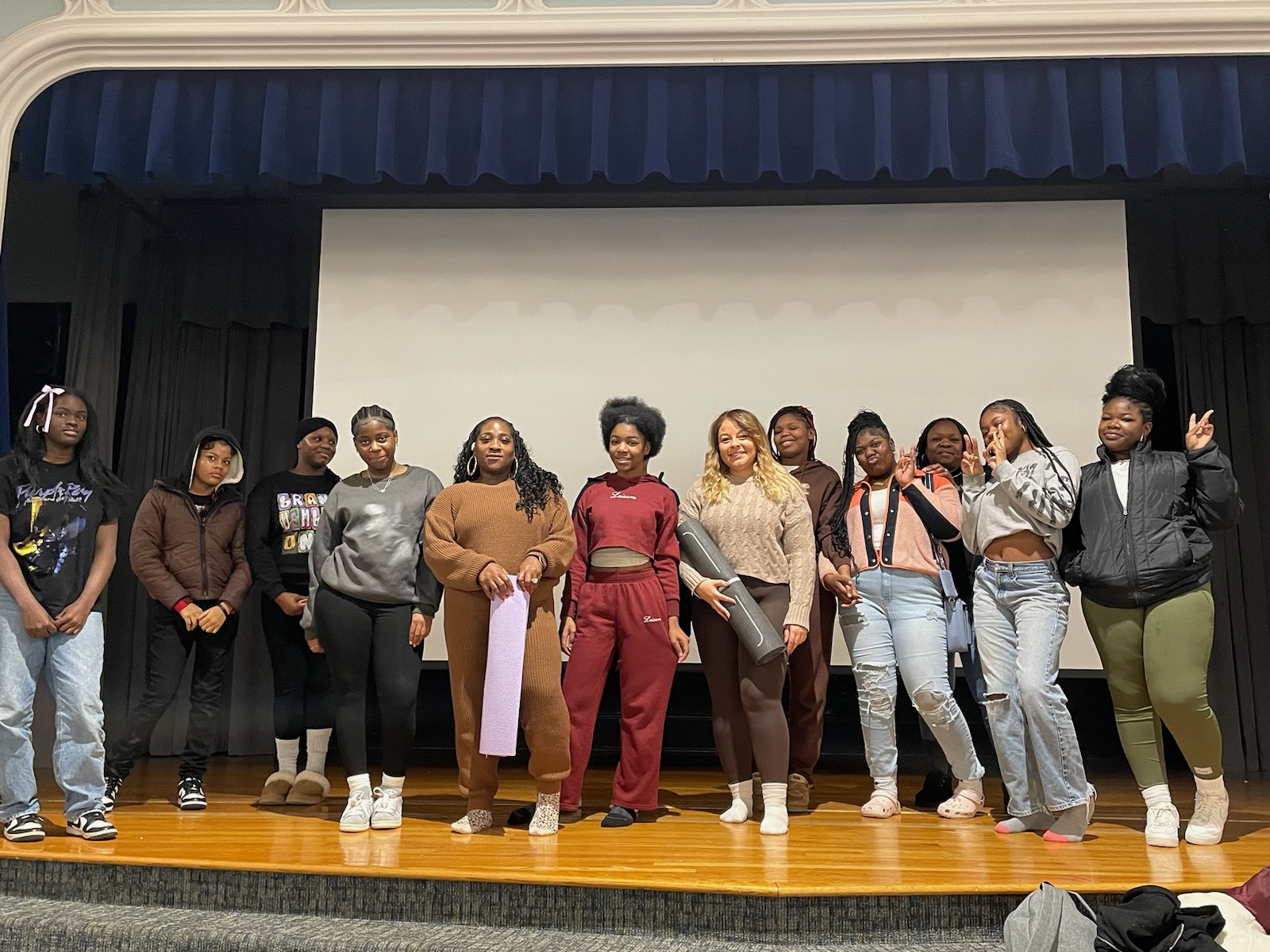 This is a photo of a group of girls standing on the stage at Syracuse STEM at Blodgett, holding yoga mats and smiling at the camera.